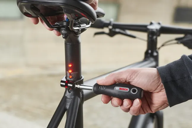 Persona che utilizza un cacciavite per regolare il reggisella di una bicicletta con spie luminose.