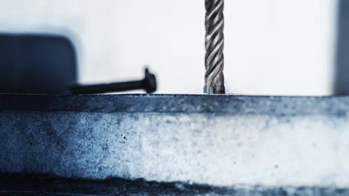 Una punta da trapano rotante che pratica un foro in una superficie metallica.