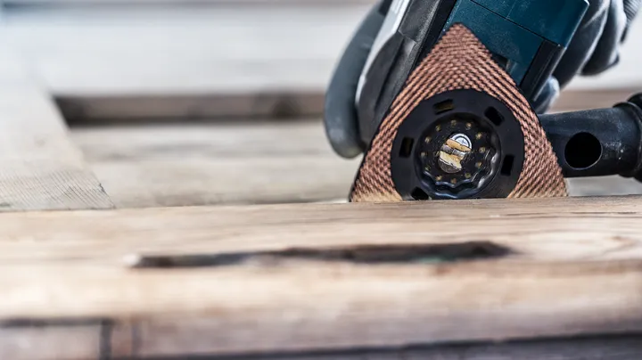 Persona che indossa dispositivi di sicurezza mentre leviga il legno con un utensile multiuso.