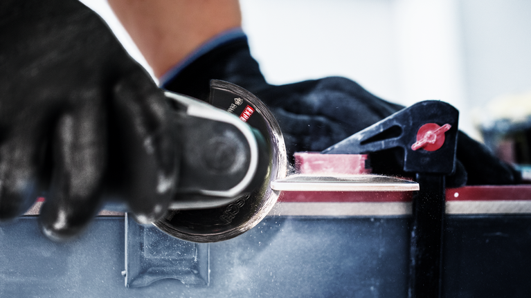 Una persona che indossa un equipaggiamento di sicurezza utilizza un utensile elettrico per tagliare una superficie dura.