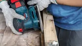 Una persona che indossa dispositivi di sicurezza lucida il legno con una levigatrice elettrica.