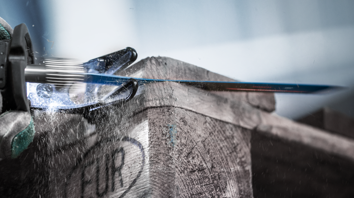 Una persona che indossa dispositivi di sicurezza usa un seghetto alternativo per tagliare una cassa di legno.