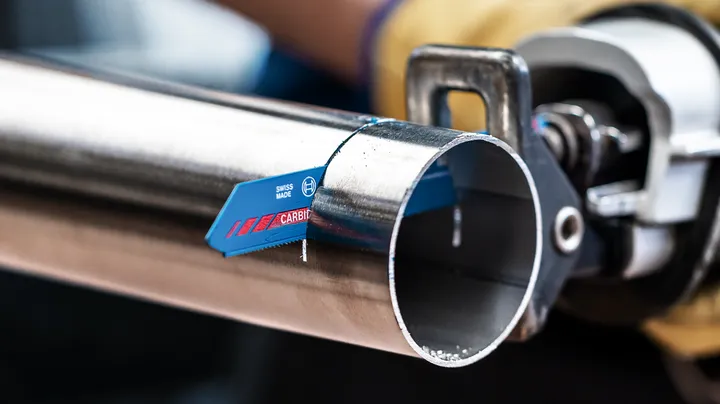 Una persona che indossa un equipaggiamento di sicurezza usa un seghetto alternativo per tagliare un tubo di metallo.