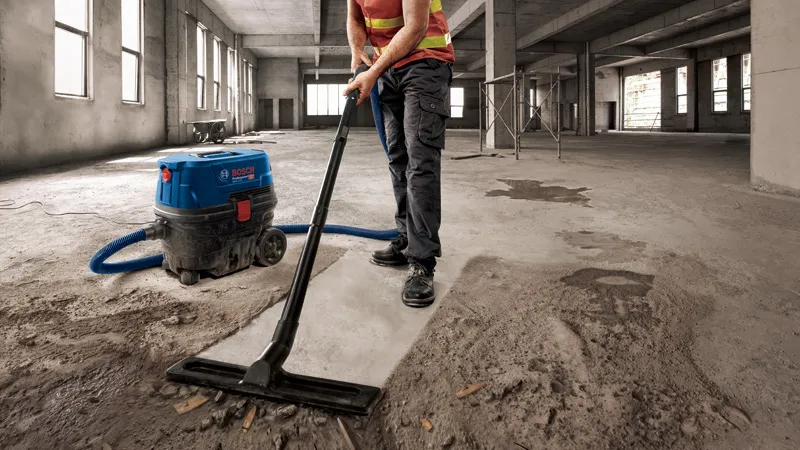 Una persona che indossa dispositivi di sicurezza aspira la polvere di cemento in un grande edificio incompiuto.