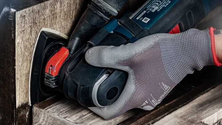 Una persona che indossa dispositivi di sicurezza leviga il pavimento in legno utilizzando una levigatrice elettrica.