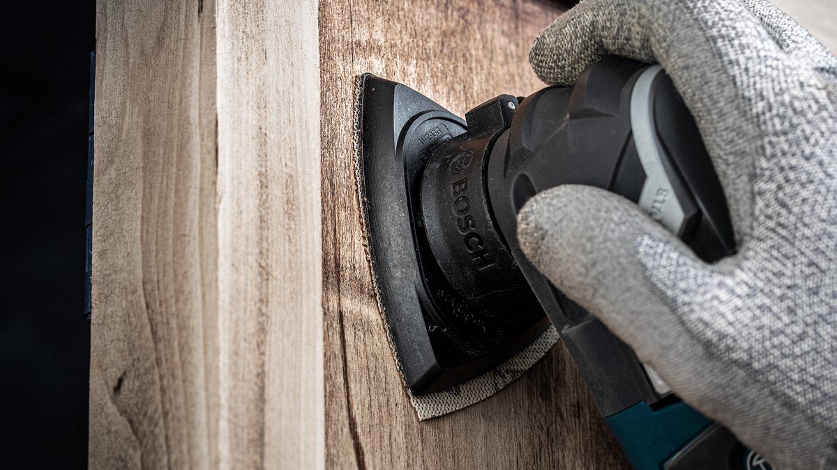 Una persona che indossa dispositivi di sicurezza leviga una superficie di legno con un utensile elettrico.