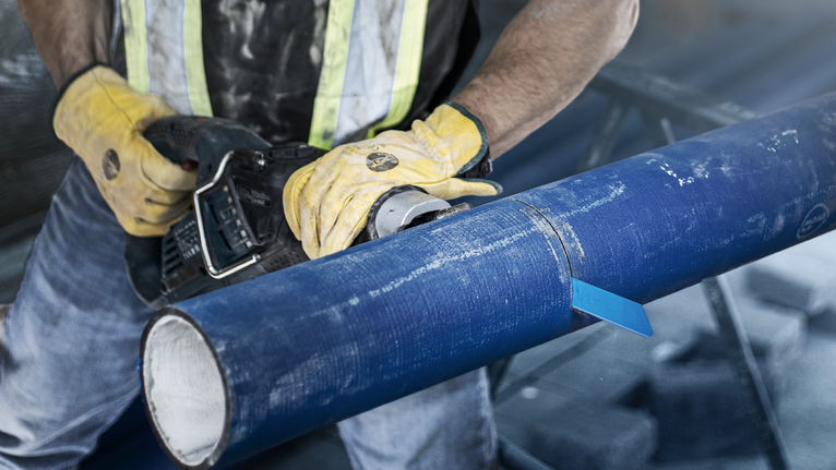 Una persona che indossa un equipaggiamento di sicurezza taglia un grande tubo blu con un elettroutensile.