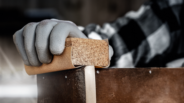 Persona che indossa dispositivi di sicurezza mentre leviga il legno con un blocco abrasivo.