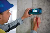 Una persona che indossa un equipaggiamento di sicurezza utilizza un ricevitore laser per tracciare delle misurazioni su un muro di cemento.