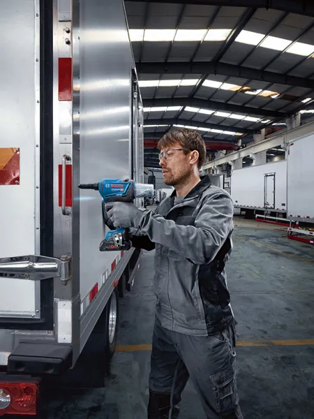 Una persona che indossa dispositivi di sicurezza utilizza una rivettatrice senza fili sulla portiera di un camion.