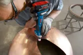 Una persona che indossa un equipaggiamento di sicurezza sfrega il bordo di una grande cupola metallica.
