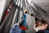 Una persona che indossa un equipaggiamento di sicurezza lavora all'interno di un tubo metallico con una smerigliatrice dritta a batteria.
