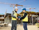 Due persone che indossano dispositivi di sicurezza discutono di un elettroutensile in un cantiere edile.