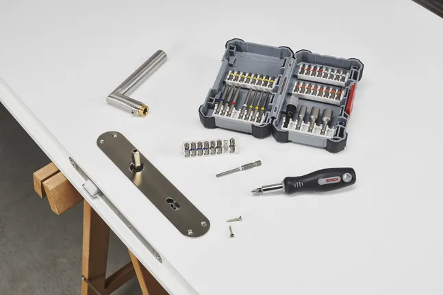 Set di cacciaviti e manico in metallo accanto a una serratura parzialmente installata su un banco da lavoro.