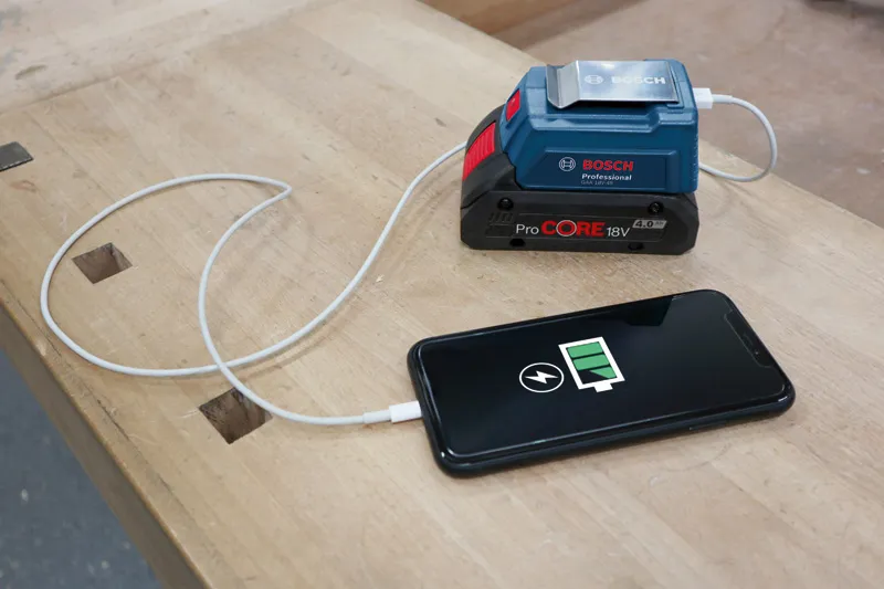 Caricabatterie portatile collegato a uno smartphone in carica su un banco da lavoro in legno.