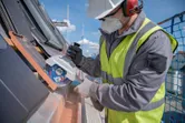 Una persona che indossa dispositivi di sicurezza utilizza una smerigliatrice angolare a batteria per tagliare le tegole.