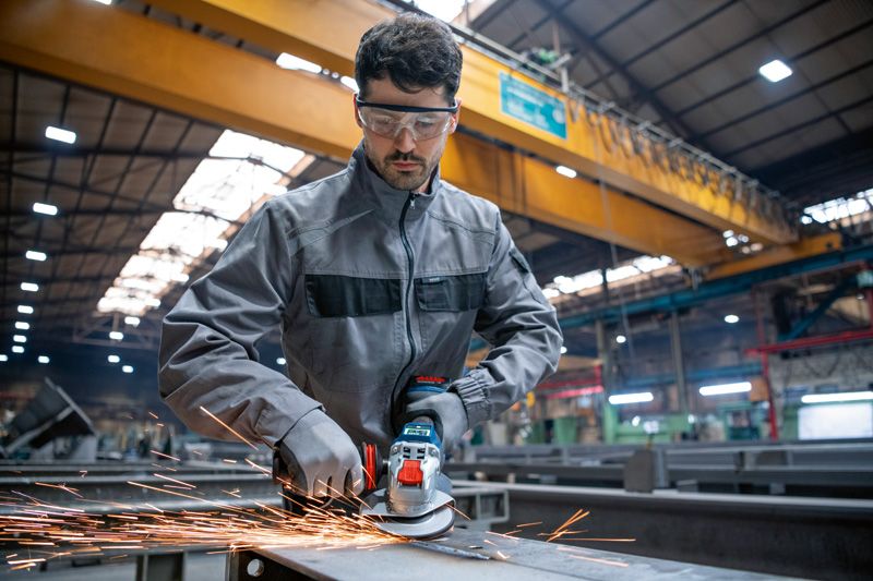 Una persona che indossa dispositivi di sicurezza lavora il metallo con una smerigliatrice angolare a batteria in una fabbrica.