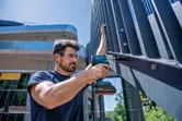 Una persona che indossa dispositivi di sicurezza utilizza una chiave a impulsi a batteria su una recinzione metallica.