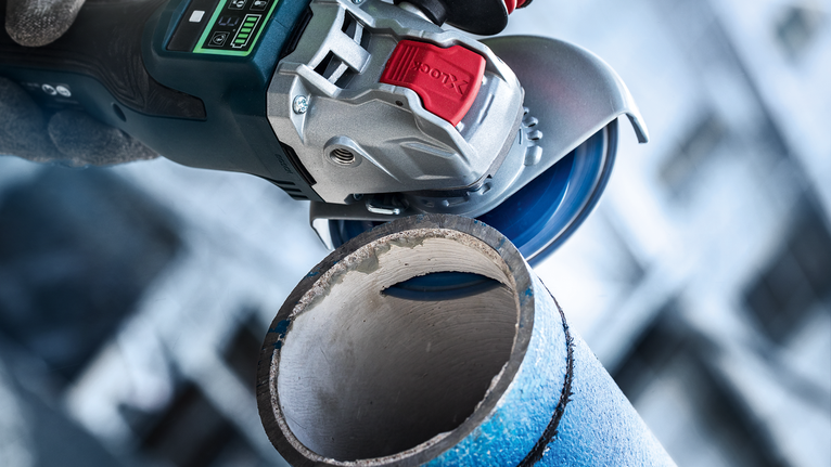 Una persona che indossa dispositivi di sicurezza utilizza una smerigliatrice angolare per tagliare un tubo metallico.