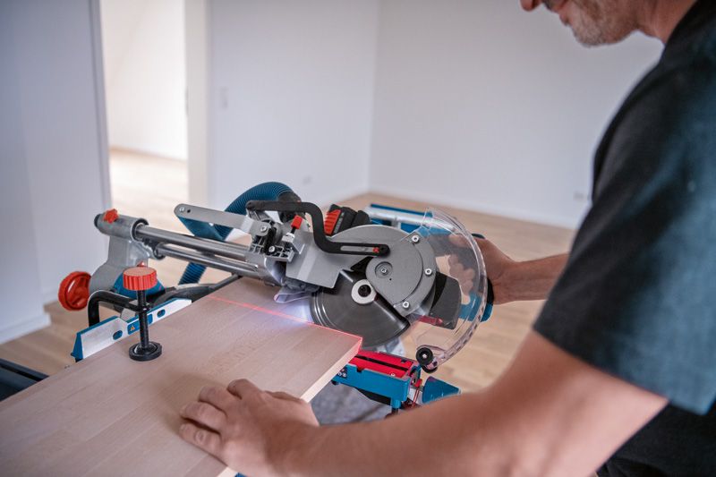 Una persona utilizza una sega troncatrice a batteria con uno strumento di livellamento laser per tagliare il legno.