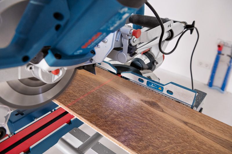 Sega troncatrice con livella laser che taglia un'asse di legno su un banco da lavoro.