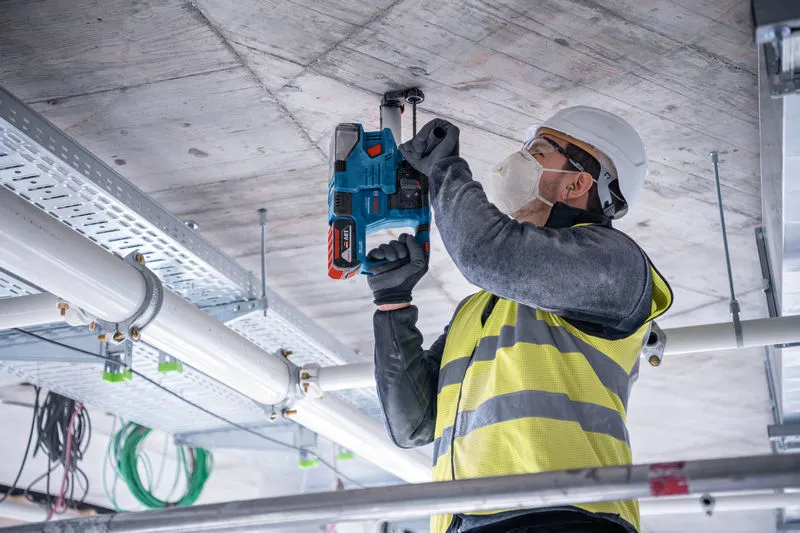 Una persona che indossa un equipaggiamento di sicurezza fora un soffitto di cemento in un cantiere edile.