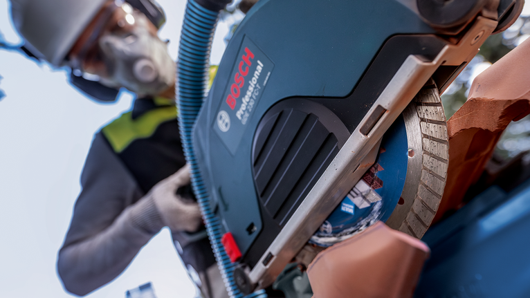 Una persona che indossa un equipaggiamento di sicurezza usa una sega circolare per tagliare un tubo di argilla.