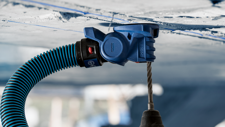 Accessorio per l'aspirazione della polvere collegato a un trapano che crea un foro in un soffitto di cemento.
