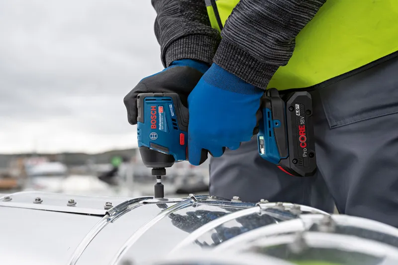 Una persona che indossa un equipaggiamento di sicurezza avvita una vite su un pezzo di metallo con un avvitatore a impulsi a batteria.