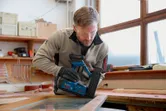 Una persona che indossa dispositivi di protezione individuale utilizza una chiodatrice pneumatica a batteria su un telaio di legno.