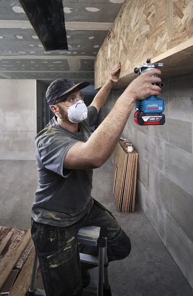 Una persona che indossa dispositivi di sicurezza utilizza una fresatrice su uno scaffale di legno.