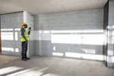 Una persona che indossa dispositivi di protezione individuale utilizza una livella laser per proiettare una linea retta su una parete.