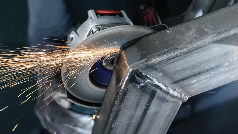 La persona che indossa l'equipaggiamento di sicurezza macina il metallo, creando scintille.