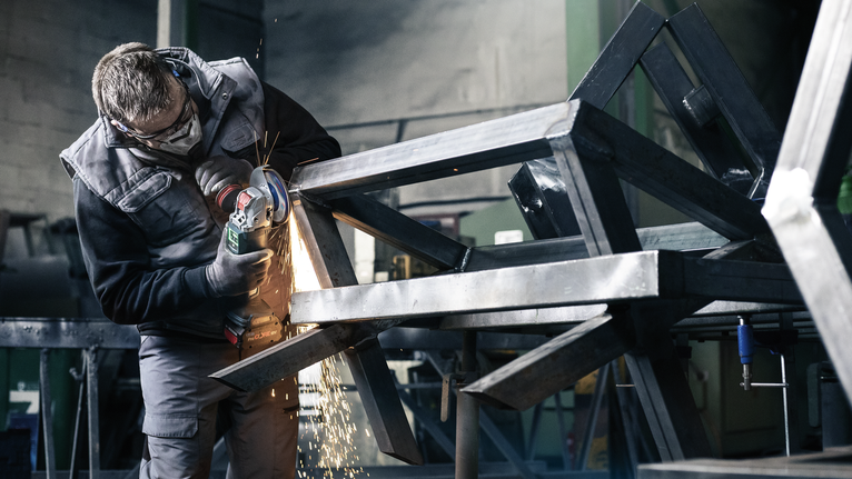 Una persona che indossa un equipaggiamento di sicurezza macina un telaio metallico, producendo scintille.