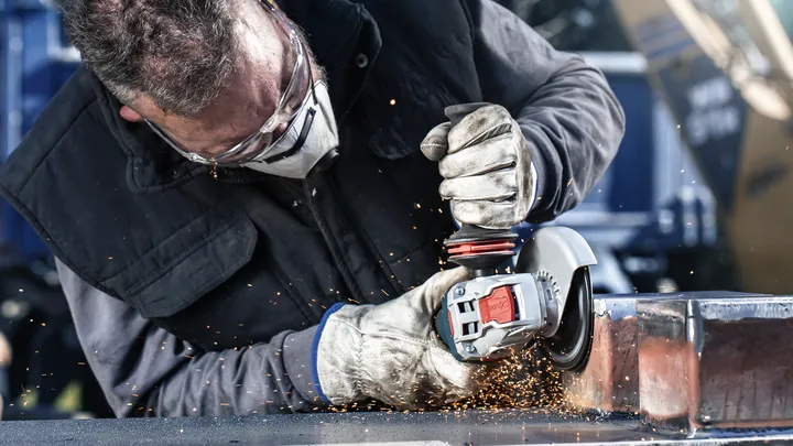 La persona che indossa l'equipaggiamento di sicurezza macina il metallo, creando scintille.