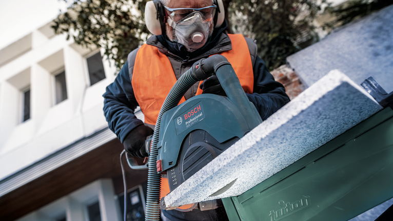 Una persona che indossa un equipaggiamento di sicurezza taglia una lastra di pietra con una grande sega circolare.