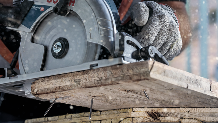 Una persona che indossa dispositivi di sicurezza taglia assi di legno con una sega circolare.