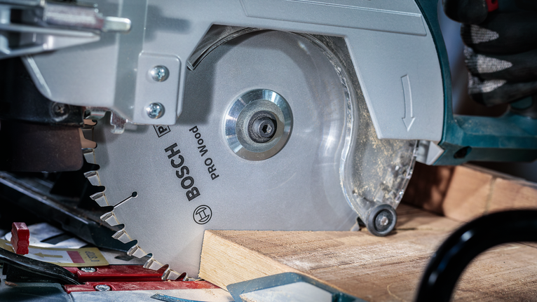 Una persona che indossa dispositivi di sicurezza aziona una sega circolare mentre taglia un'asse di legno.