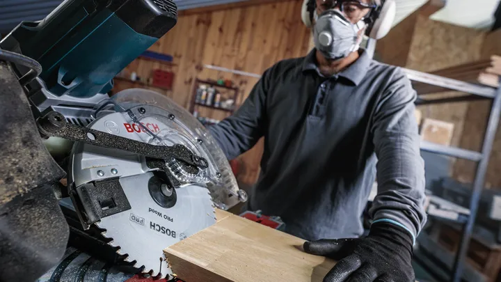 Persona che indossa dispositivi di sicurezza mentre taglia il legno con una sega circolare in un'officina.