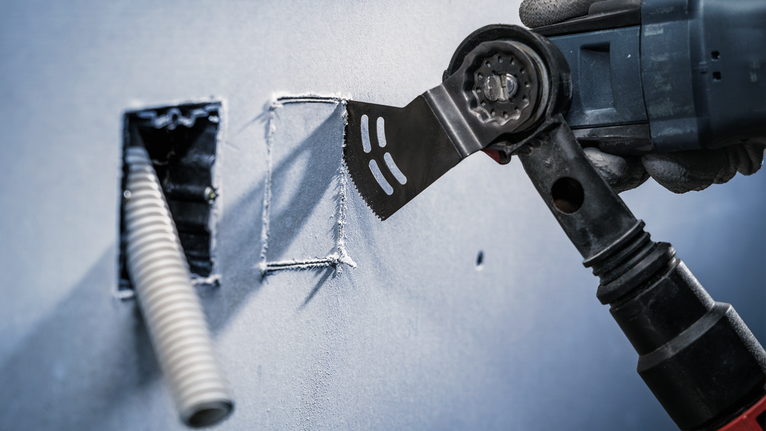 Una persona che indossa un equipaggiamento di sicurezza pratica un taglio netto nel muro a secco con un utensile multiuso.