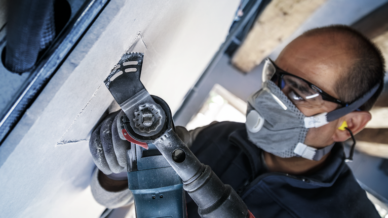 Una persona che indossa un equipaggiamento di sicurezza taglia il cartongesso con un utensile elettrico.