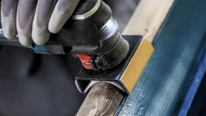 Persona che indossa dispositivi di sicurezza mentre leviga il legno con un utensile elettrico multifunzione.