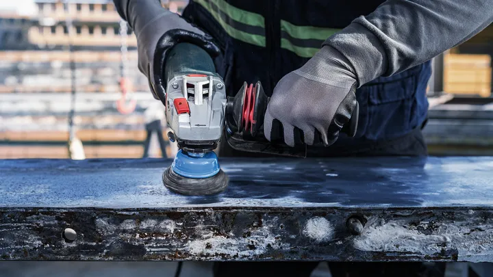 Una persona che indossa un equipaggiamento di sicurezza lucida una superficie metallica con un utensile elettrico.