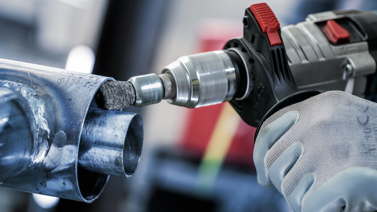 Una persona che indossa dispositivi di sicurezza utilizza un trapano elettrico per levigare l'interno di un tubo metallico.
