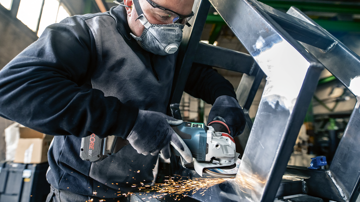 Una persona che indossa un equipaggiamento di sicurezza macina un telaio metallico, producendo scintille.