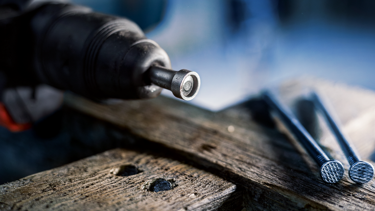 Utensile elettrico che inserisce un elemento di fissaggio nel legno accanto a diversi chiodi di grandi dimensioni.