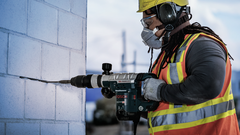 Una persona che indossa l'equipaggiamento di sicurezza perfora un muro di blocchi di cemento.