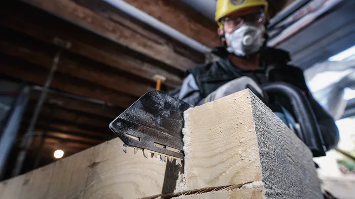 Una persona che indossa dispositivi di sicurezza taglia del legname spesso con una sega elettrica.