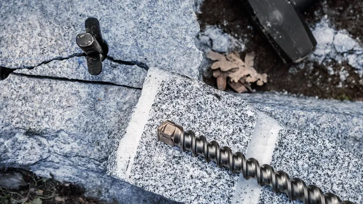 Grande punta da trapano e cuneo su un blocco di granito crepato in un cantiere edile.