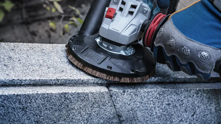 Una persona che indossa un equipaggiamento di sicurezza lucida la pietra con un utensile elettrico.